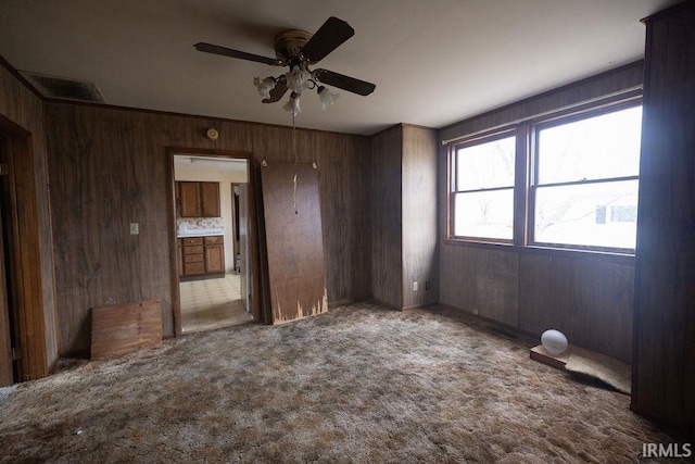 unfurnished room featuring carpet flooring, ceiling fan, and wood walls