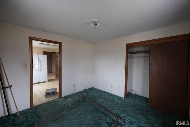 unfurnished bedroom featuring a closet, dark carpet, and white fridge with ice dispenser