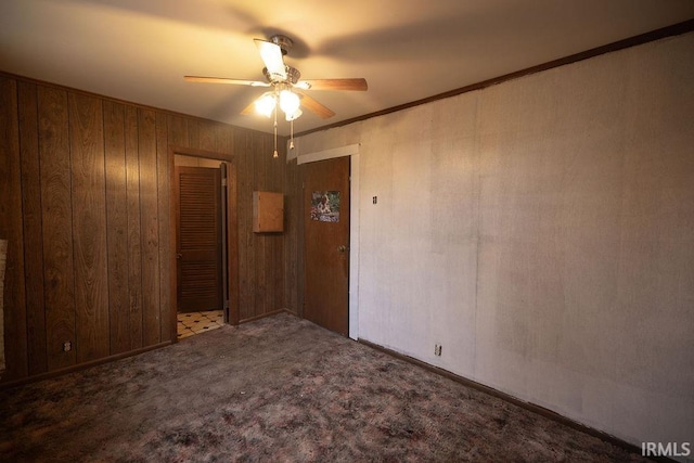 carpeted spare room featuring ceiling fan, ornamental molding, and wood walls