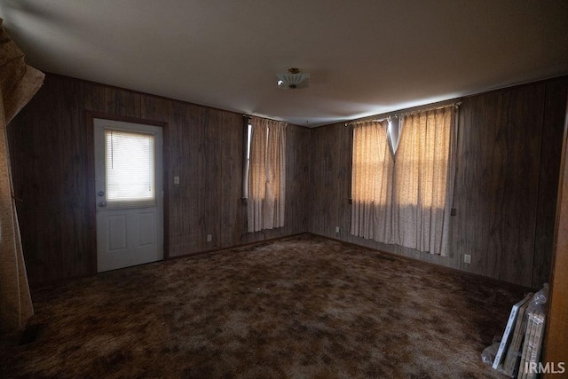 interior space featuring wooden walls and dark colored carpet