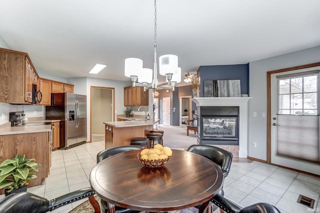 dining space with sink, a notable chandelier, light tile patterned flooring, and a multi sided fireplace