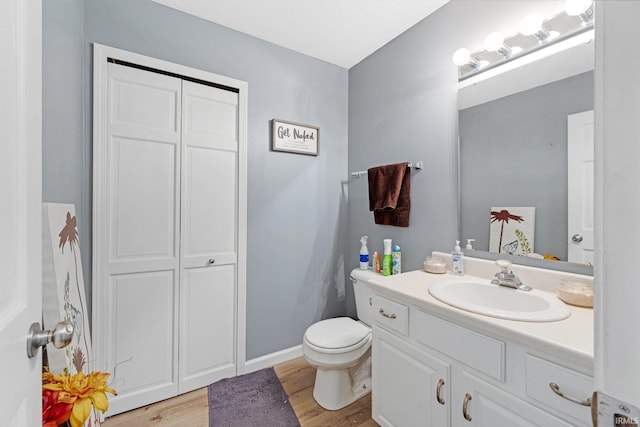 bathroom featuring toilet, a closet, wood finished floors, and vanity