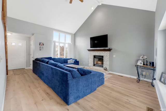 living area featuring high vaulted ceiling, a fireplace, visible vents, baseboards, and light wood-style floors