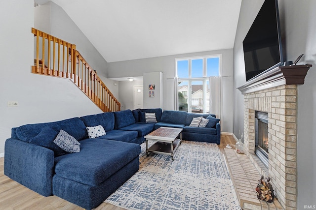 living room featuring a brick fireplace, baseboards, stairway, and wood finished floors