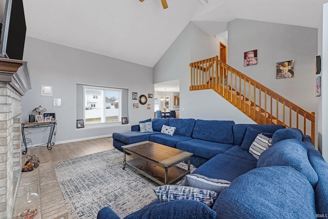 living room with high vaulted ceiling, ceiling fan with notable chandelier, wood finished floors, baseboards, and stairway