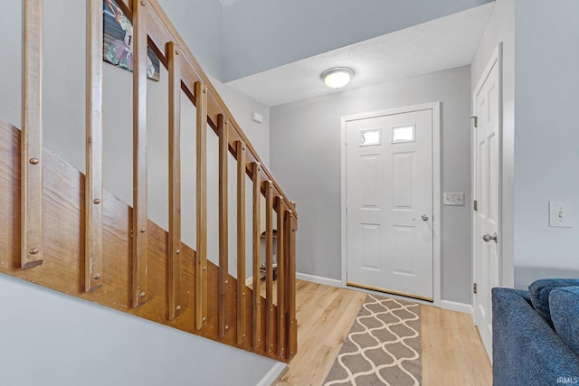 entrance foyer with light wood-style floors, stairs, baseboards, and a textured ceiling