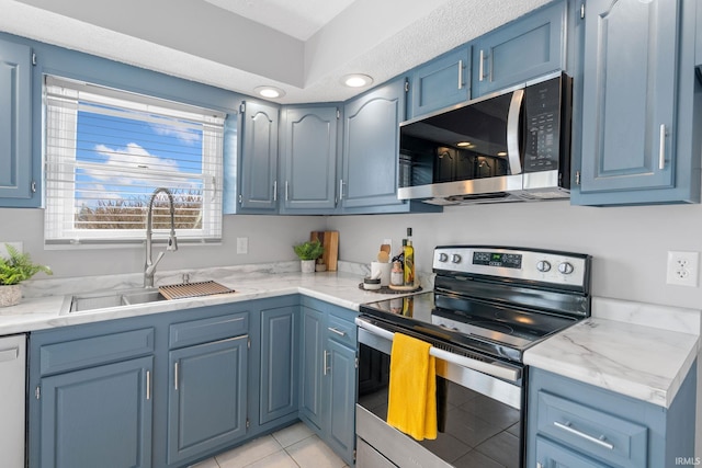 kitchen with light tile patterned flooring, blue cabinets, sink, stainless steel appliances, and light stone countertops