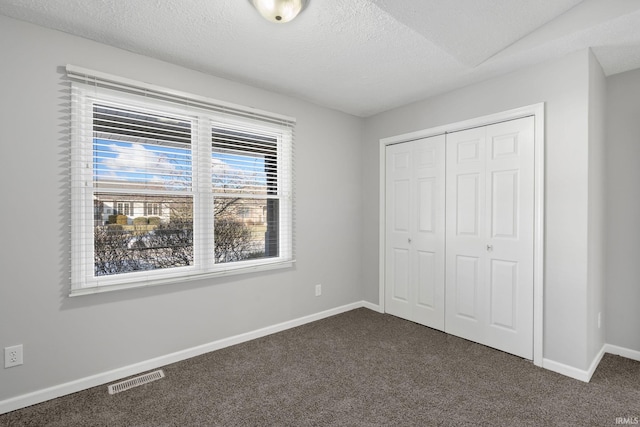 unfurnished bedroom with dark carpet, a closet, and a textured ceiling