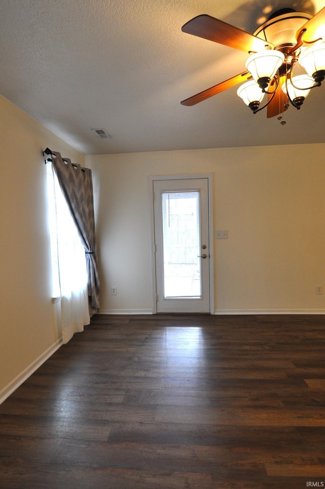 empty room with baseboards, a textured ceiling, visible vents, and dark wood-style flooring