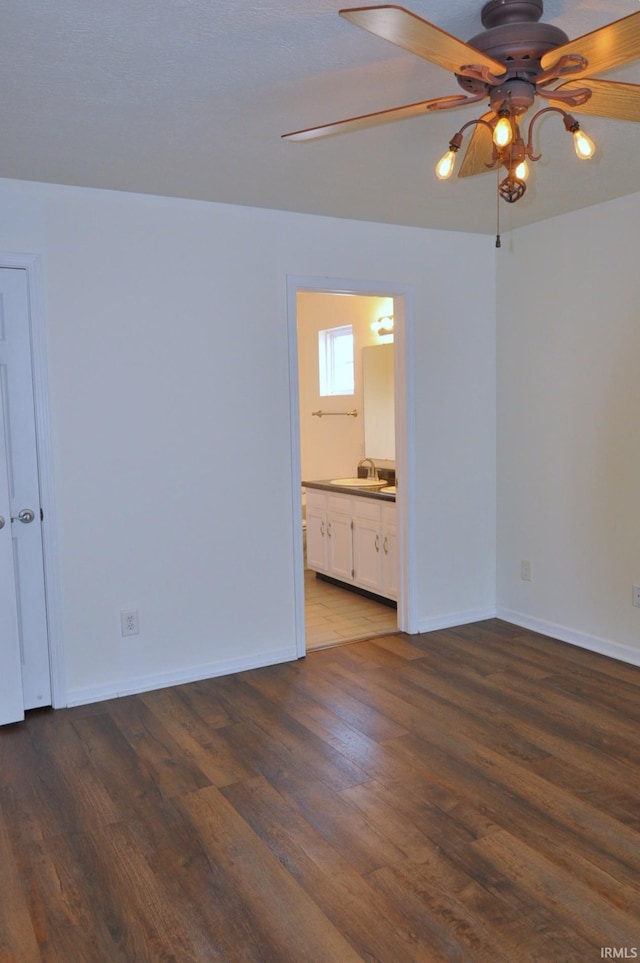 unfurnished bedroom featuring a sink, ensuite bath, baseboards, and wood finished floors