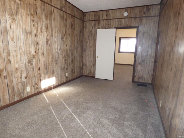 carpeted spare room with wooden walls and a textured ceiling