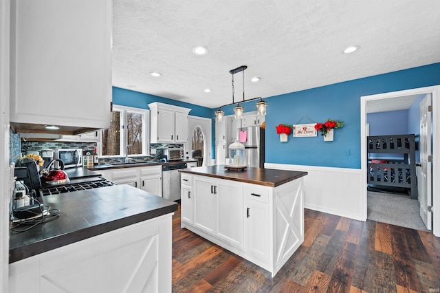 kitchen with butcher block countertops, white cabinetry, decorative light fixtures, a center island, and stainless steel appliances