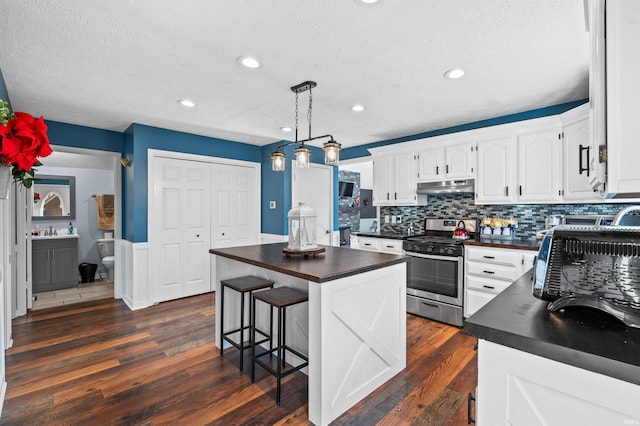 kitchen featuring stainless steel gas range oven, a center island, hanging light fixtures, dark hardwood / wood-style flooring, and white cabinets