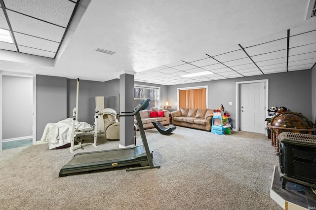 exercise area with a paneled ceiling, carpet floors, and a wood stove