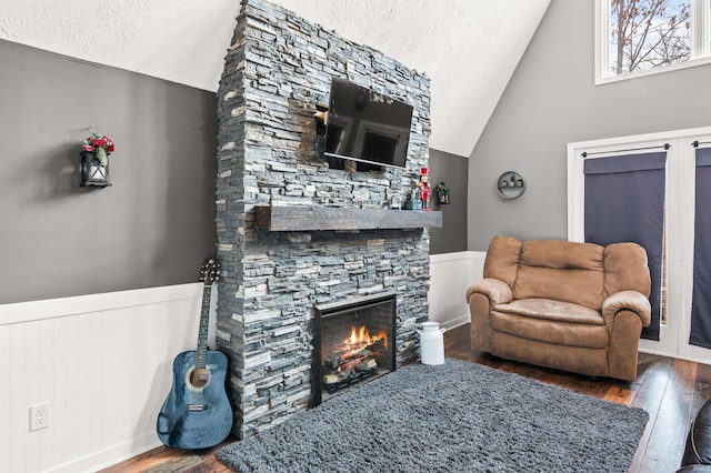 living room with hardwood / wood-style flooring, vaulted ceiling, and a stone fireplace