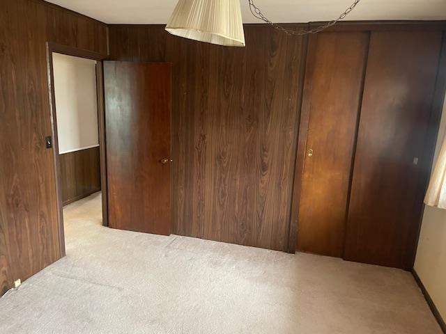 bedroom with light colored carpet, wooden walls, and a closet