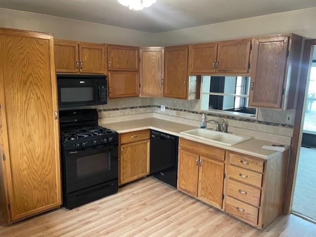 kitchen with tasteful backsplash, sink, black appliances, and light wood-type flooring