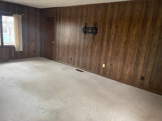 carpeted spare room with a textured ceiling and wood walls