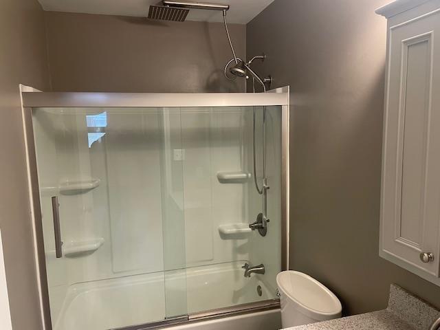 bathroom with combined bath / shower with glass door and toilet