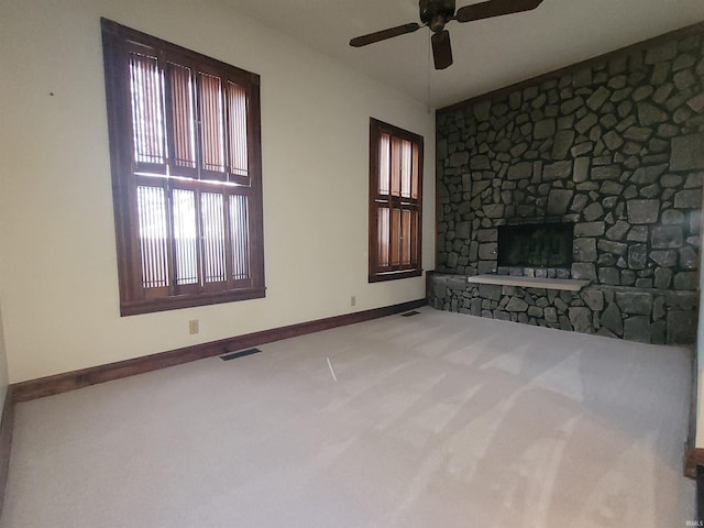 unfurnished living room with ceiling fan, light colored carpet, and a stone fireplace