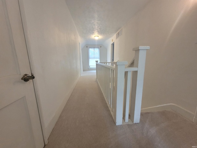 hallway featuring light colored carpet, lofted ceiling, and a textured ceiling