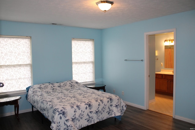 bedroom featuring ensuite bathroom, dark hardwood / wood-style flooring, and a textured ceiling