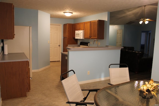 kitchen featuring stove, ceiling fan, kitchen peninsula, light carpet, and a textured ceiling