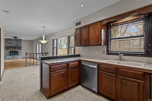 kitchen featuring pendant lighting, sink, a brick fireplace, stainless steel dishwasher, and kitchen peninsula