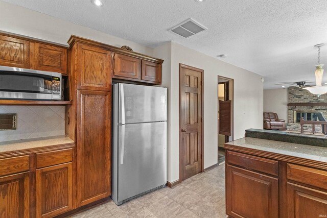 kitchen featuring appliances with stainless steel finishes, decorative backsplash, hanging light fixtures, a brick fireplace, and a textured ceiling