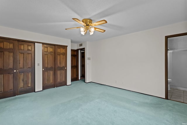 unfurnished bedroom featuring ensuite bathroom, light colored carpet, ceiling fan, and a textured ceiling