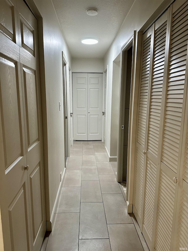 corridor with light tile patterned flooring and a textured ceiling