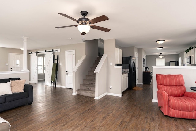 living room with dark wood-type flooring, decorative columns, a barn door, and ceiling fan