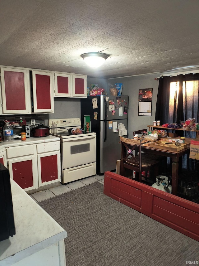 kitchen with white electric range oven, a textured ceiling, light tile patterned floors, stainless steel refrigerator, and white cabinets