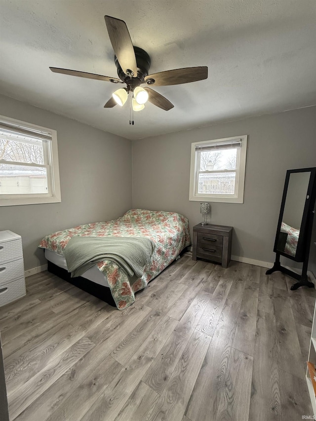 bedroom with ceiling fan, multiple windows, and light hardwood / wood-style flooring