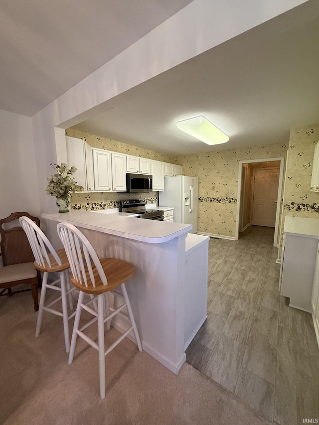 kitchen with white cabinetry, stainless steel appliances, kitchen peninsula, and a kitchen bar