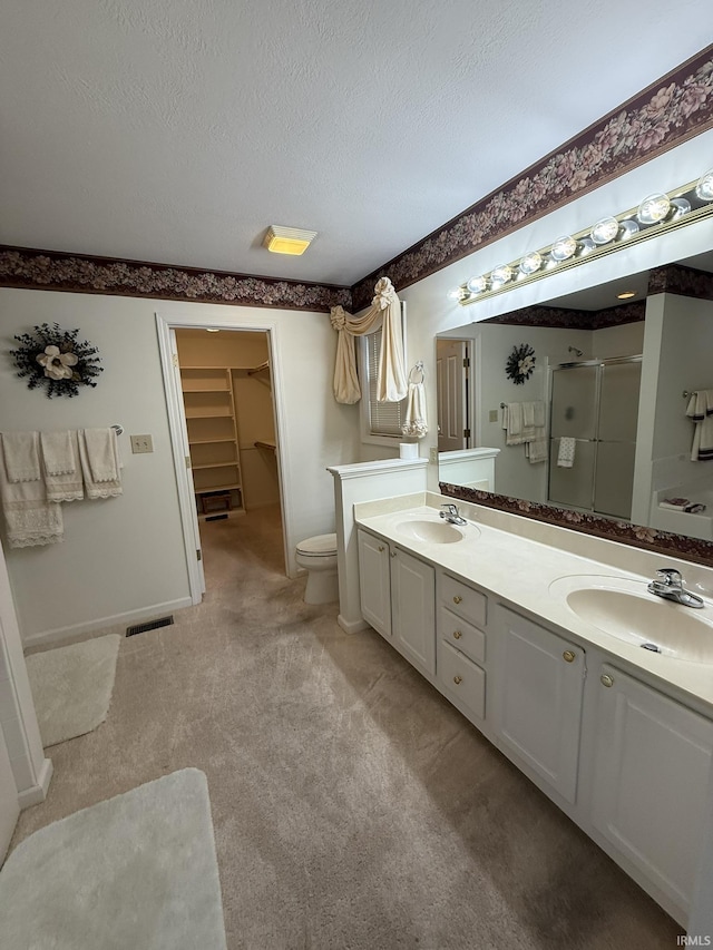 bathroom with vanity, toilet, a textured ceiling, and a shower with shower door