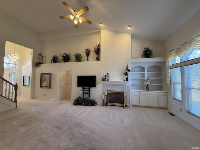 unfurnished living room with ceiling fan with notable chandelier, high vaulted ceiling, carpet floors, and a tile fireplace