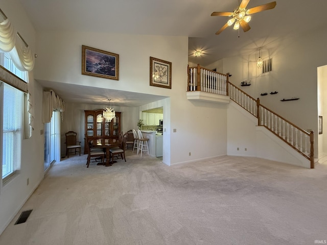 unfurnished living room featuring light colored carpet, ceiling fan with notable chandelier, and a towering ceiling