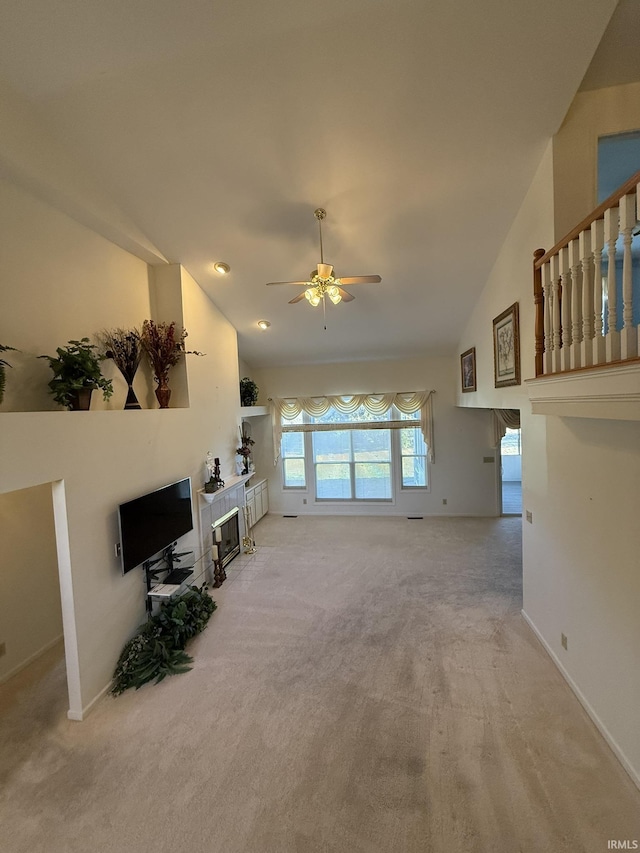 living room with ceiling fan, a tiled fireplace, high vaulted ceiling, and light carpet