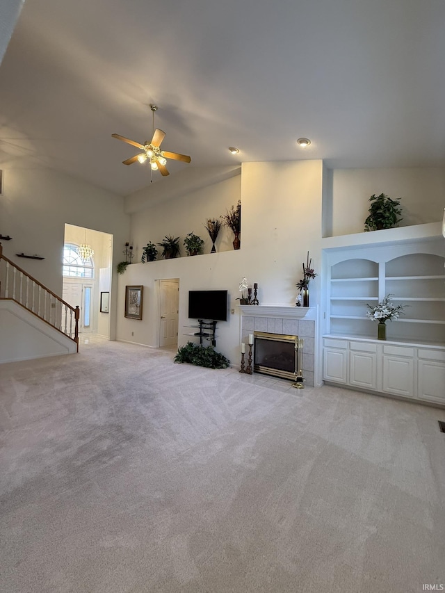 unfurnished living room with a tiled fireplace, light carpet, ceiling fan, and built in shelves