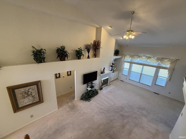 living room with a tiled fireplace, vaulted ceiling, light colored carpet, and ceiling fan