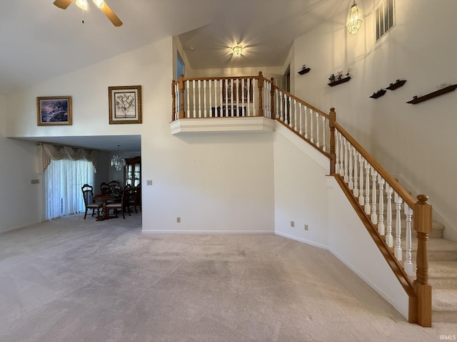 unfurnished living room featuring ceiling fan, carpet floors, and a high ceiling