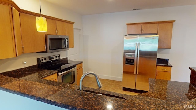 kitchen featuring sink, dark stone countertops, kitchen peninsula, pendant lighting, and stainless steel appliances