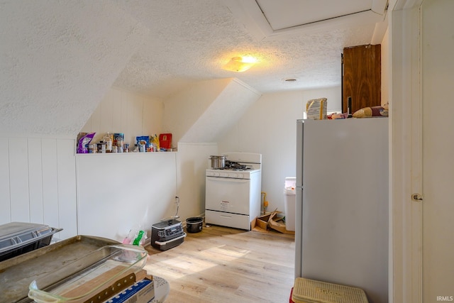 interior space featuring lofted ceiling, white appliances, light hardwood / wood-style floors, and a textured ceiling