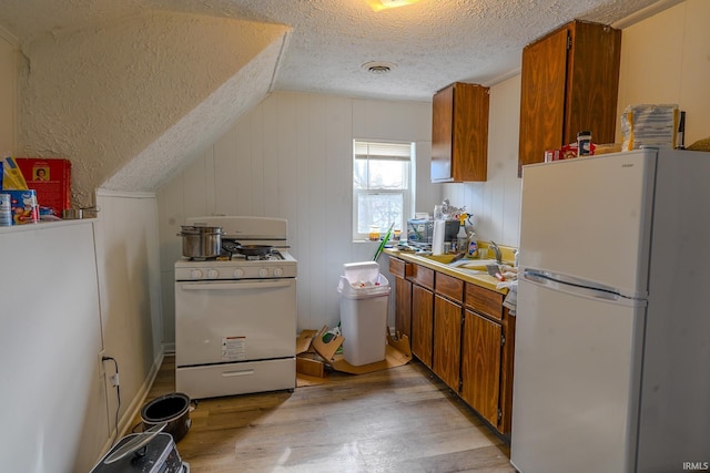 kitchen featuring sink, vaulted ceiling, a textured ceiling, light wood-type flooring, and white appliances