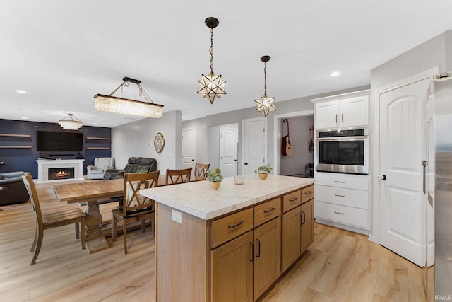 kitchen with pendant lighting, white cabinetry, a center island, stainless steel oven, and light hardwood / wood-style floors