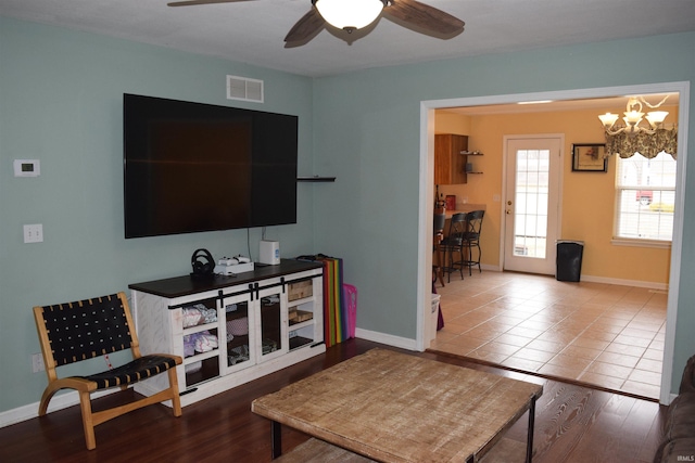 tiled living room with ceiling fan with notable chandelier