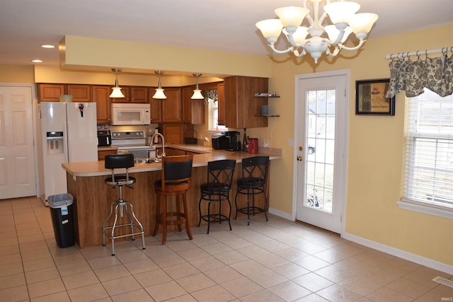 kitchen with hanging light fixtures, a breakfast bar, white appliances, and kitchen peninsula