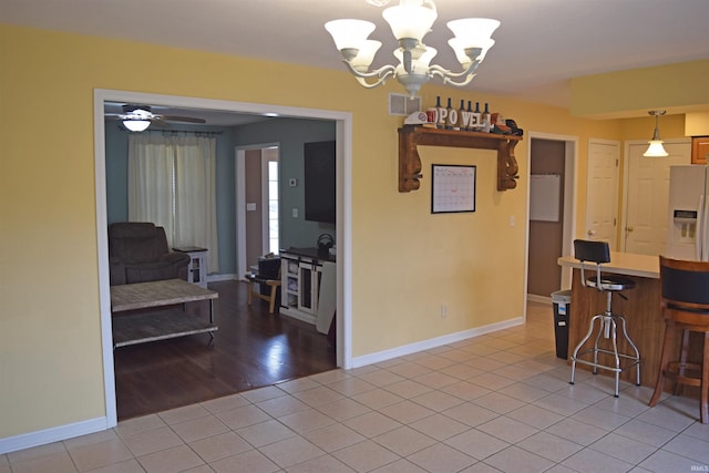 kitchen with tile patterned floors, fridge with ice dispenser, hanging light fixtures, a kitchen breakfast bar, and ceiling fan with notable chandelier