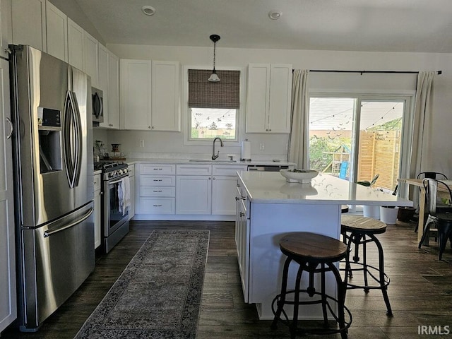 kitchen with appliances with stainless steel finishes, white cabinetry, a healthy amount of sunlight, a kitchen bar, and decorative light fixtures